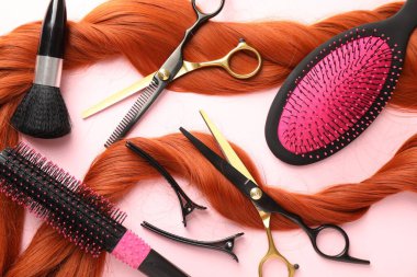 Açık pembe zemin üzerinde saç teli ve kuaför aletleri, düz uzanma