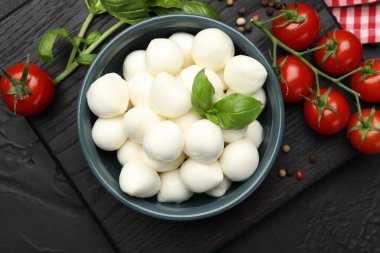 Lezzetli mozzarella peynir topları kasede, fesleğende, biberlikte ve domateslerde siyah masada, üst tarafta.