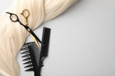 Farklı kuaför aletleri ve açık gri arka planda sarı saç kilidi. Metin için boşluk