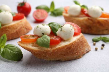 Mozarella peynirli sandviçler, açık gri masada domates ve fesleğen, yakın plan.