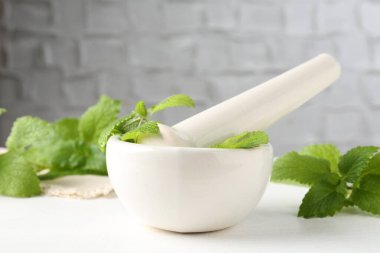 Taze limon merhemi yaprakları ve beyaz ahşap masada havan topuzu, yakın plan.