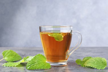 Cam bardakta Aromatik limon merhemi çayı ve gri desenli masada taze yapraklar.