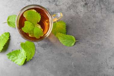 Cam bardakta Aromatik limon merhemi çayı ve gri desenli masa üzerinde taze yapraklar, düz yatak. Metin için boşluk