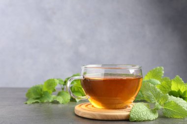 Cam fincanda aromatik limon merhemi çayı ve gri masada taze yapraklar, mesaj için yer.