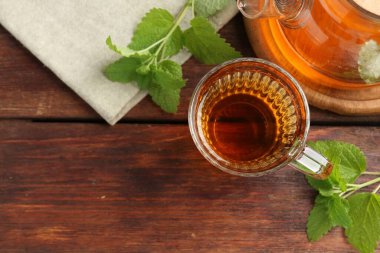 Cam fincanda aromatik limon merhemi çayı, çaydanlık ve ahşap masada taze yapraklar. Metin için boşluk