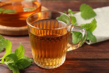 Cam fincanda aromatik limon merhemi çayı, çaydanlık ve ahşap masada taze yapraklar, yakın plan.