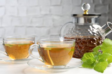 Cam fincanlarda aromatik limon merhemi çayı, çaydanlık ve beyaz masada taze yapraklar, yakın plan.