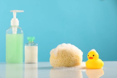 Şirin plastik ördekler, köpük, sünger ve açık mavi arka planda duran kozmetik ürünler.