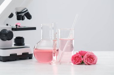 Lüks parfüm yapıyorum. Temel yağlar cam eşyalar, çiçekler ve mikroskop beyaz ahşap masa üzerinde, yakın çekim