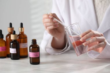 Laboratuvarda beyaz ahşap masada lüks parfüm üreten profesyonel bir parfümcü.