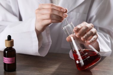 Laboratuardaki ahşap masada lüks parfüm üreten profesyonel parfümcü.