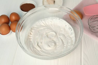 Krem şantili kase, çırpma ve malzemeler beyaz ahşap masada, yakın plan.