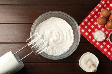 Krem şantili kase, el çırpıcısı ve malzemeler ahşap masada, düz yerde.