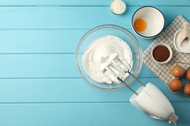 Krem şantili kase, el mikseri ve malzemeler açık mavi ahşap masa, düz yatıyordu.