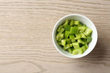 Tahta masadaki kasede taze yeşil dolmalık biber parçaları. Metin için boşluk