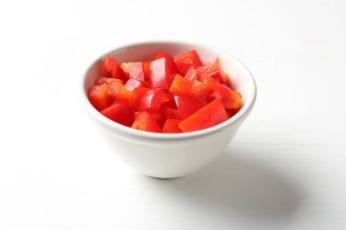 Beyaz ahşap masada kasede taze kırmızı dolma biber parçaları, yakın plan.