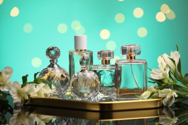 Ayna yüzeyinde birçok farklı parfüm şişesi ve çiçek bulanık ışıklı turkuaz arka planda, yakın plan