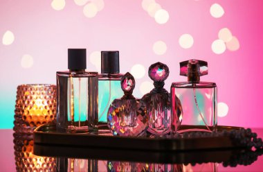 Ayna yüzeyinde birçok farklı parfüm şişesi ve aksesuar var. Pembe arka planda, bulanık ışıklar, yakın plan.