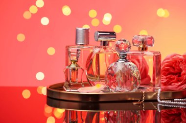 Farklı parfüm şişeleri, aksesuarlar ve çiçekler ayna yüzeyinde kırmızı arka planda bulanık ışıklarla, yakın plan