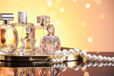 Ayna yüzeyinde turuncu arka planda birçok farklı parfüm şişesi ve aksesuar var.