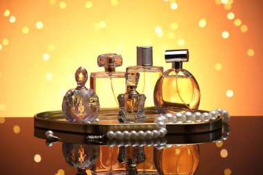Ayna yüzeyinde turuncu arka planda birçok farklı parfüm şişesi ve aksesuar var.