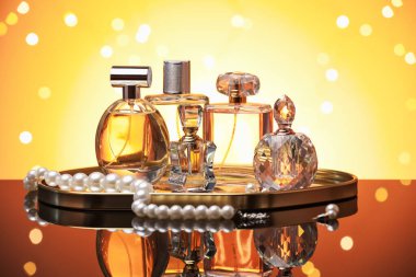 Ayna yüzeyinde turuncu arka planda birçok farklı parfüm şişesi ve aksesuar var.