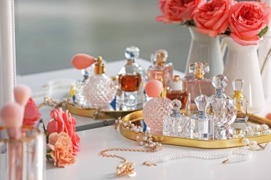 Farklı parfüm şişeleri, aksesuarlar ve çiçekler kapalı salonda.