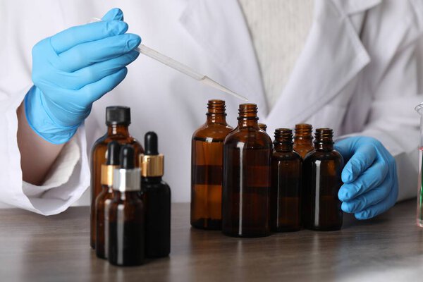 Профессиональный парфюмер разрабатывает роскошные духи за деревянным столом в лаборатории, крупным планом