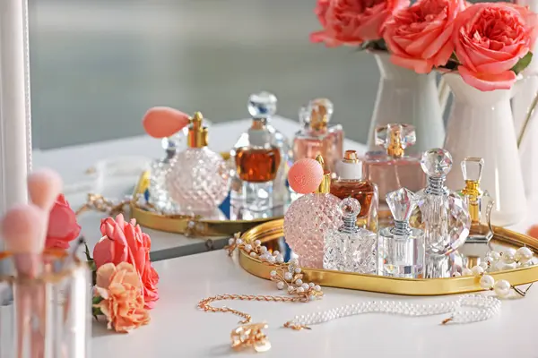 Farklı parfüm şişeleri, aksesuarlar ve çiçekler kapalı salonda.