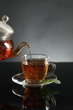 Koyu ayna masasında çaydanlıktan fincana taze demlenmiş çay dökülüyor.