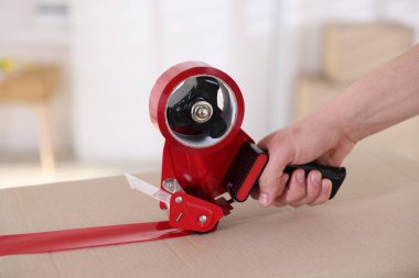 Karton kutuyu kapalı bir yere kapatmak için yapıştırıcılı bant kullanan bir adam.