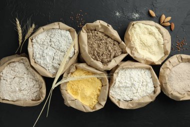 Siyah masa üzerinde, kağıt torbalarda farklı tipte un, düz yerde.