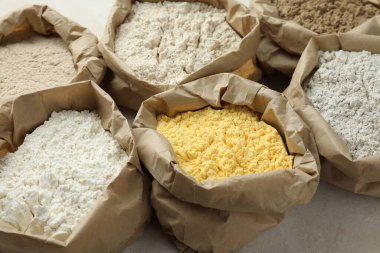 Beyaz masadaki kağıt torbalarda farklı türde un, yakın plan.