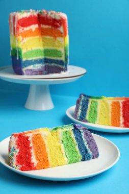 Lezzetli gökkuşağı pastası parçaları açık mavi masada, yakın plan.