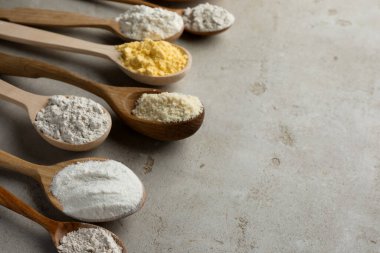 Açık gri masadaki kaşıklarda farklı türde un, yakın plan. Metin için boşluk