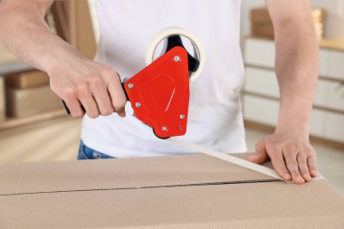 Karton kutuyu kapalı bir yere kapatmak için yapıştırıcılı bant kullanan bir adam.