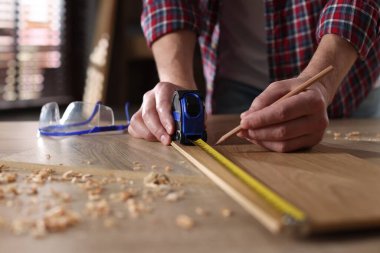 Kapalı alanda bant ile ahşap kalas ölçen bir adam.