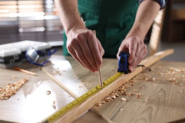 İçerideki ahşap masada bant ve kalemle tahta ölçen adam, yakın plan.
