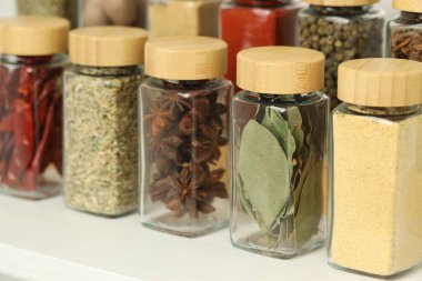 Beyaz masadaki kavanozlardaki farklı aromatik baharatlar, yakın plan.