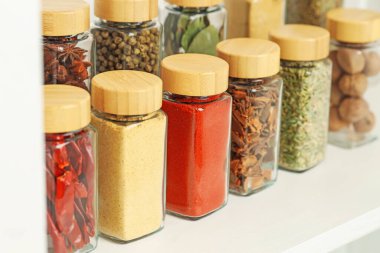 Kapalı alandaki beyaz raflardaki kavanozlardaki farklı aromatik baharatlar.