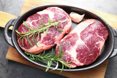 Gri masadaki fırında pişirme kabında çiğ et ve baharat parçaları.