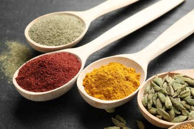 Siyah masada kaşıklardaki farklı aromatik baharatlar, yakın plan.