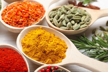 Beyaz ahşap masadaki kaşıklarda farklı aromatik baharatlar, yakın plan.