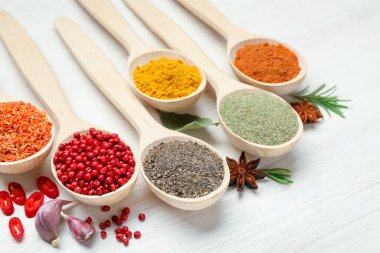 Beyaz ahşap masadaki kaşıklarda farklı aromatik baharatlar, yakın plan.