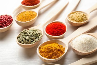 Beyaz ahşap masadaki kaşıklarda farklı aromatik baharatlar, yakın plan.