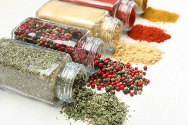 Beyaz masadaki kavanozlarda farklı aromatik baharatlar, yakın plan.