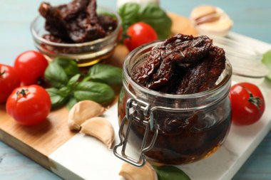 Lezzetli güneşte kurutulmuş domatesler, taze sebzeler, fesleğen ve sarımsak mavi ahşap masada, yakın plan.