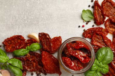 Lezzetli güneşte kurutulmuş domatesler kavanozda ve baharatlar gri desenli masada, düz yerde. Metin için boşluk