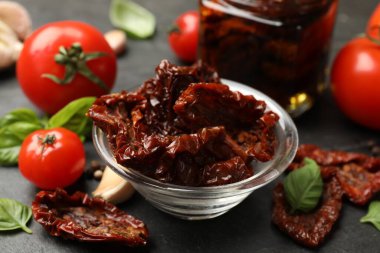 Lezzetli güneşte kurutulmuş domatesler ve taze sebzeler siyah masada, yakın plan.