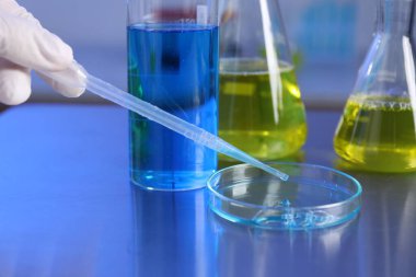 Bilim adamı, laboratuardaki masada petri kabından pipetle numune alıyor, yakın plan.